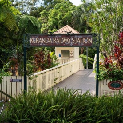 The entrance to Kuranda Railway Station with a cream picket fence and lush grenery.
